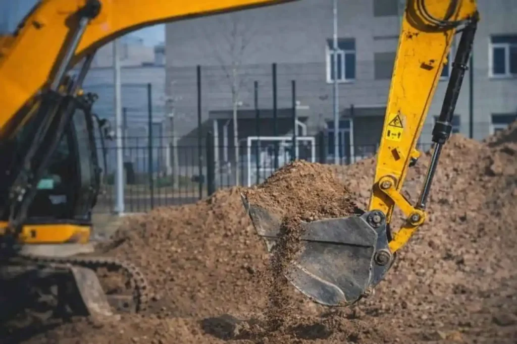Close-up of excavator bucket moving soil at an earthworks Sydney construction site with residential buildings in the background.