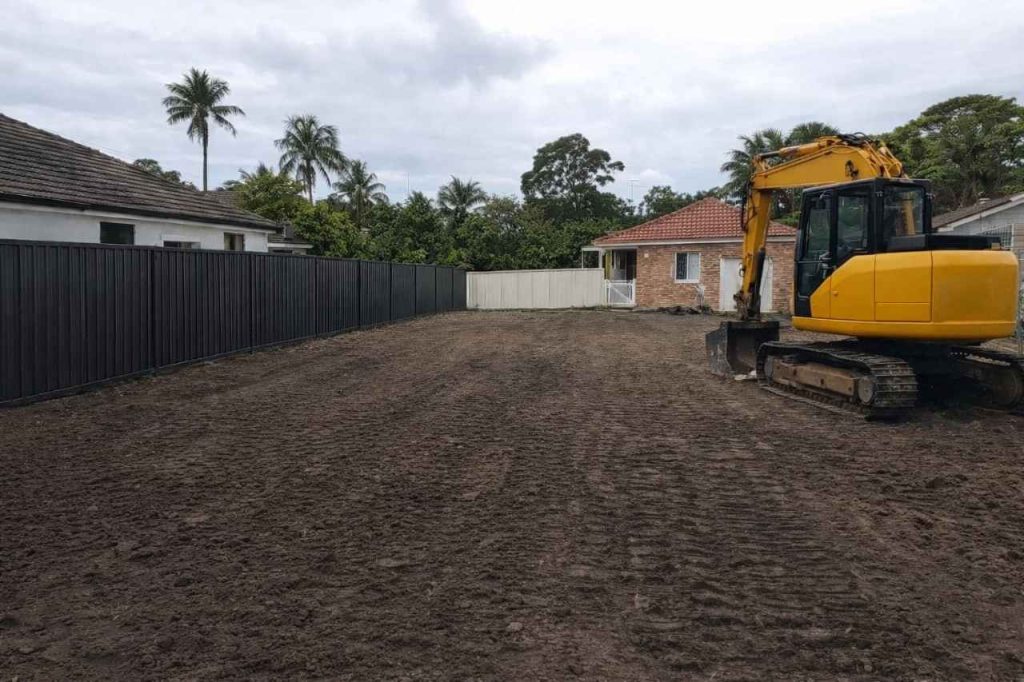 Excavator on freshly cleared residential demolition site in Sydney with levelled soil and boundary fencing.